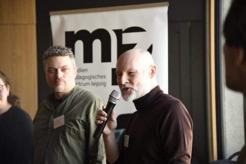 Mehrere Personen stehen nebeneinander vor einer Wand mit projiziertem mpz-Logo, eine Person spricht in ein Mikrofon